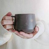 朝、両手であたたかいカップを両手で持つ女性。