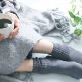 冷房で体が冷えている。ひざ掛けと温かい飲み物を飲む女性