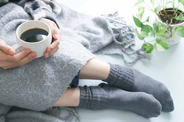 冷房で体が冷えている。ひざ掛けと温かい飲み物を飲む女性