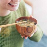 朝、女性がしょっぱそうなお味噌汁を飲もうとしている。