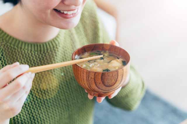 朝、女性がしょっぱそうなお味噌汁を飲もうとしている。