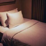 白い寝具が整えられた静かな寝室。柔らかな光が枕とシーツを照らし、穏やかな夜の静けさを感じさせる