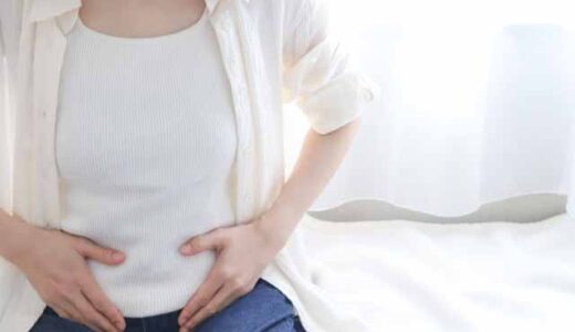 女性が朝、ベットの上でお腹を押さえている。便秘のイメージ。