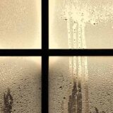 夕方、窓に雨が降りつけている。窓のガラスにはたくさんの水滴がついていて、外と中の寒暖差がある。